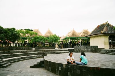 People sitting by building against sky