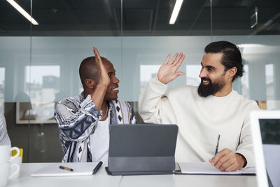 Smiling coworkers sitting at business meeting and giving each other high five