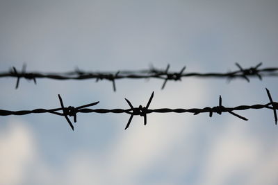 Low angle view of barbed wire fence against sky