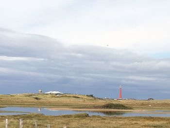 Lighthouse on field by sea against sky