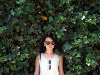 Portrait of young woman wearing sunglasses standing by plants