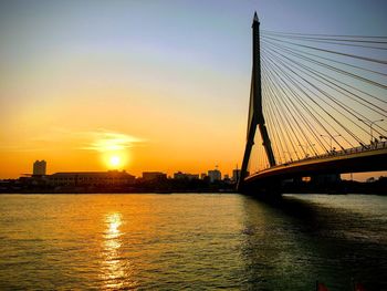 Silhouette bridge over river against sky during sunset