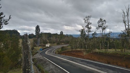 Road by trees on landscape against sky