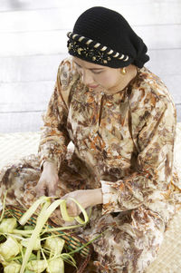 High angle view of woman weaving leaves while sitting in gazebo