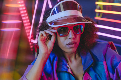 Young woman wearing retro visor and sunglasses in front of neon light