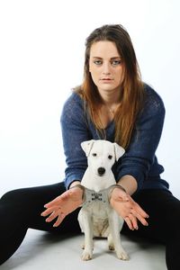 Portrait of handcuffed young woman sitting with dog against white background