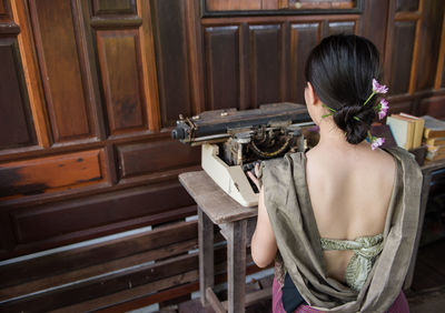 Rear view of woman in traditional clothing using typewriter at home