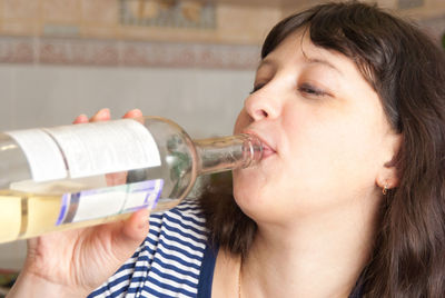 Close-up of woman drinking from bottle at home