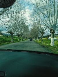 Road amidst bare trees against sky seen through car windshield