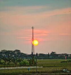 Electricity pylon on field against sky during sunset