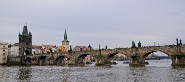 Bridge over river by buildings against sky