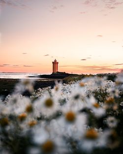 Lighthouse by sea against sky during sunset