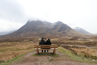 Rear view of couple sitting on bench against mountains