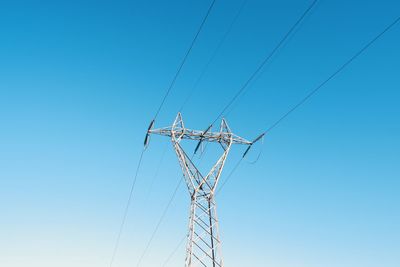 Low angle view of electricity pylon against clear blue sky