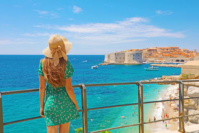 Woman standing on railing by sea against sky