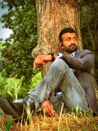 Thoughtful mid adult man sitting by tree trunk