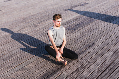 High angle view of man practicing yoga on boardwalk during sunny day