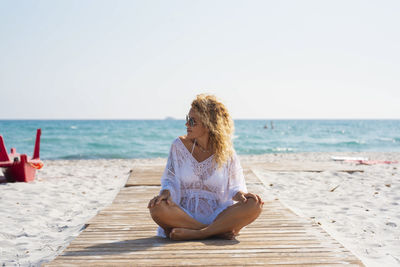 Side view of woman sitting on beach against clear sky