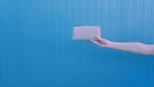 Cropped image of hand holding purse against blue wall 