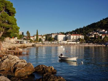 Boats moored in river by town against clear blue sky