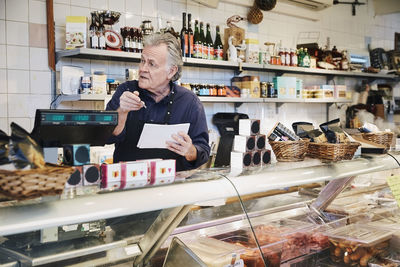 Male owner looking away while holding pen and note pad at counter in store