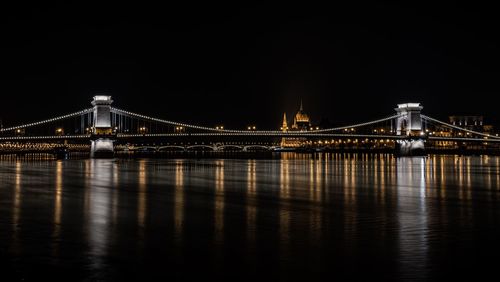 Illuminated bridge over river against sky at night