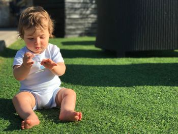Cute baby boy sitting on grassy field
