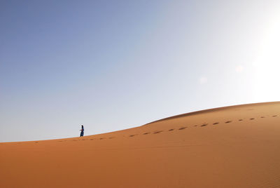 Person walking on sand dune against sky