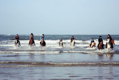 People riding horses in sea against clear sky