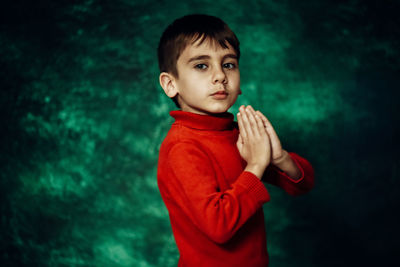 Portrait of cute boy praying against green background