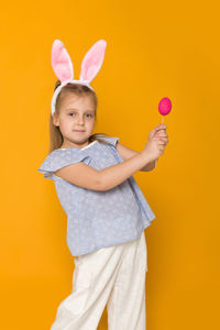 Portrait of smiling woman holding heart shape against yellow background