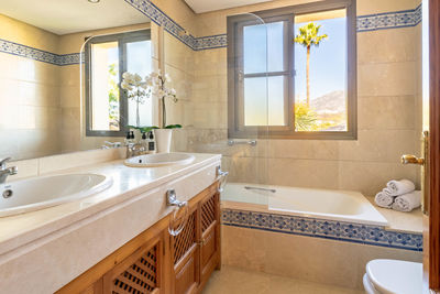 A image of a bathroom with a double sink with views overlooking a palm tree and mountain of marbella