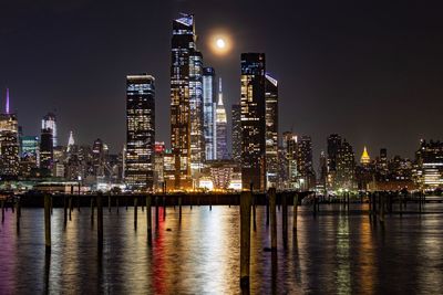 Illuminated buildings by river against sky at night