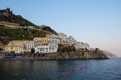 Buildings by sea against clear sky