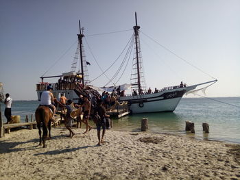 People on sailboats by sea against clear sky