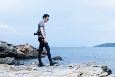 Side view of young man standing on rocky shore