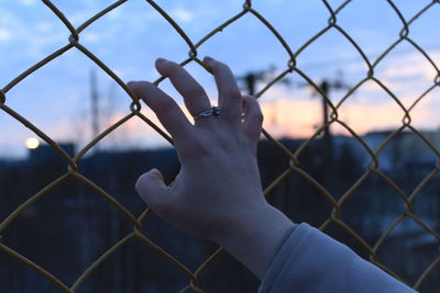 Midsection of person against sky seen through chainlink fence