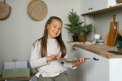 Beautiful girl holds a plate of christmas cookies in her hands in the kitchen