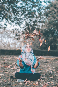 Young woman playing with dry leaves while sitting on field