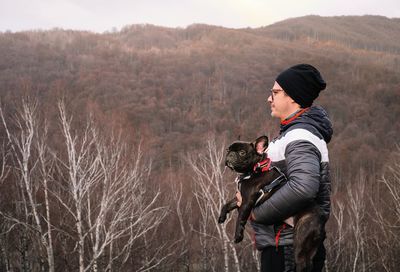 Rear view of man with french bulldog dog on land against winter mountain