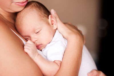 Midsection of mother holding sleepy newborn baby at home