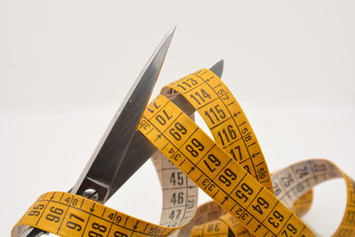 Close-up of scissors with tape measure against white background