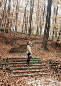 Full length portrait of young woman on stone stairs in forest, autumn, fall.