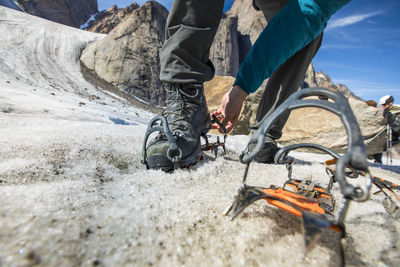 Climber straps on crampons to his mounatineering boots on glacier.