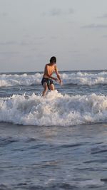 Side view of young man surfing in sea against sky