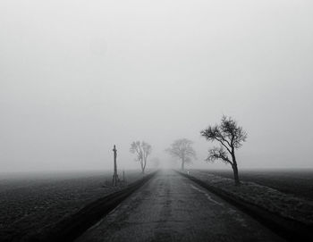 Empty road along trees on landscape against sky