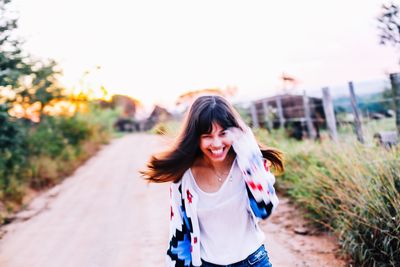 Portrait of happy young woman running on road amidst plants against clear sky