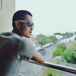 Rear view of man wearing sunglasses standing by railing in balcony