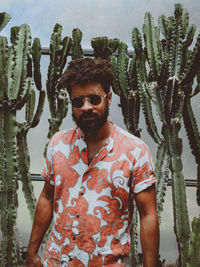 Portrait of young man wearing sunglasses standing against plants