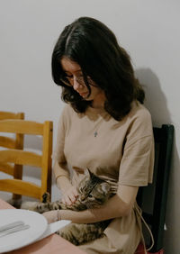 A teenage girl with a cat in her arms sits at the table.